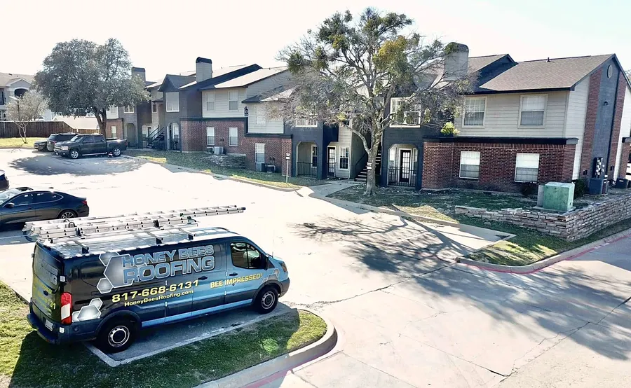 A Honey Bees Roofing van parked at a two-story apartment complex