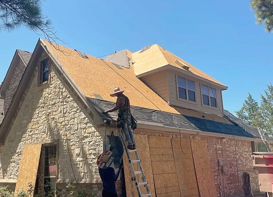 A roofer on a ladder working over new decking on a stone home