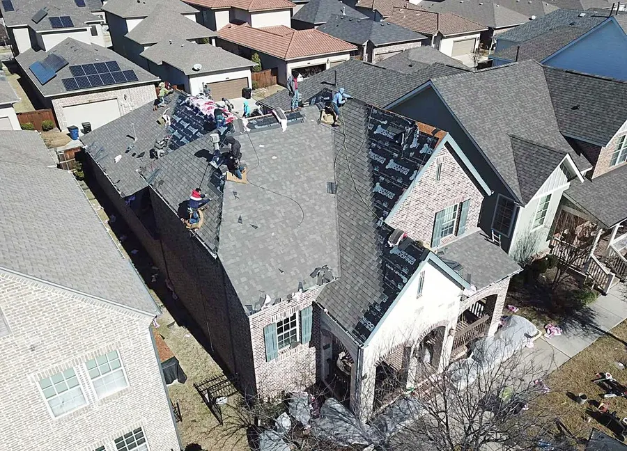 A crew replacing the roof on a two-story brick home, photographed by drone