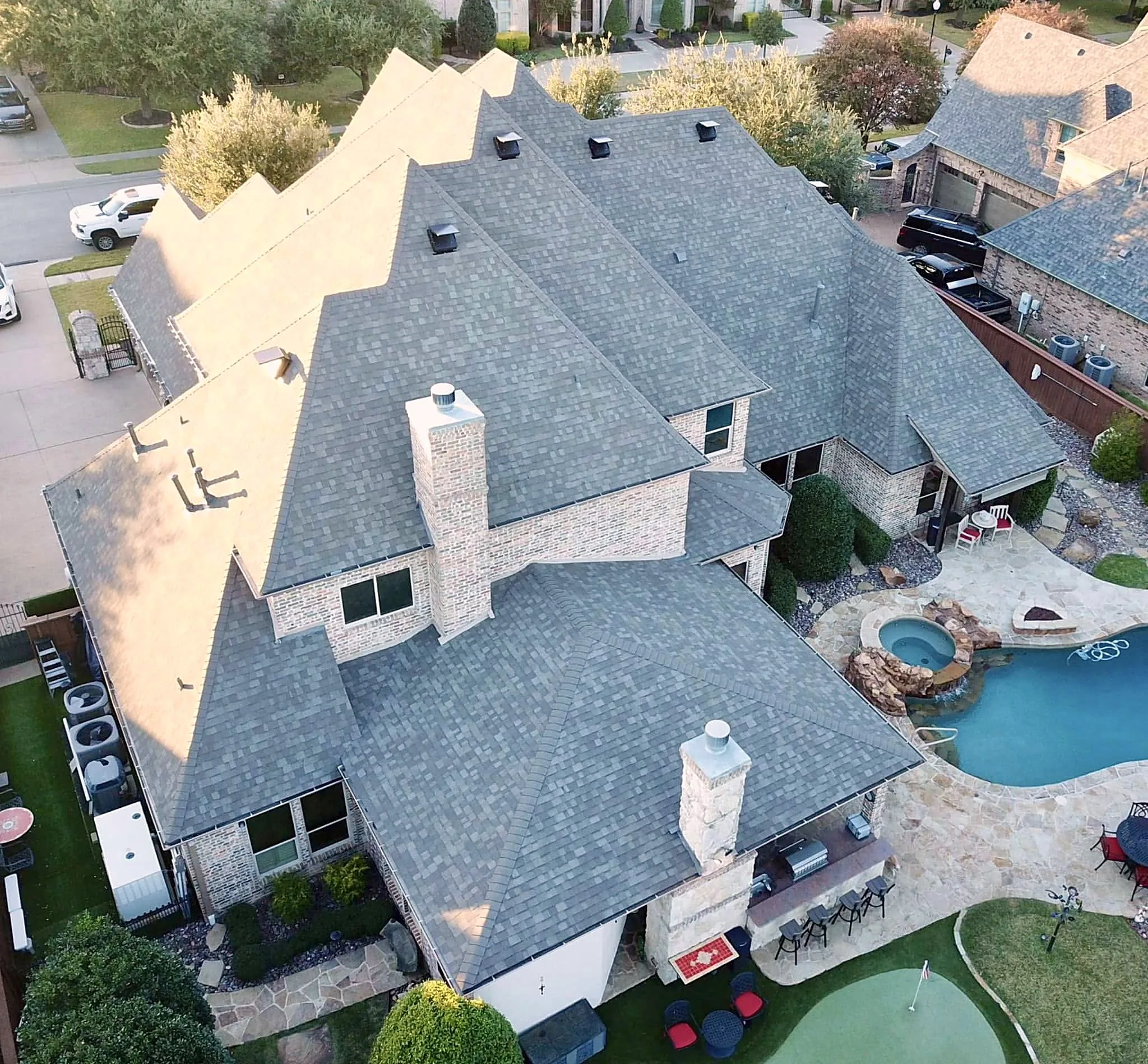 A finished Honey Bees Roofing reroof on a large brick home, photographed by drone, with new gray shingles on every slope and the pool behind