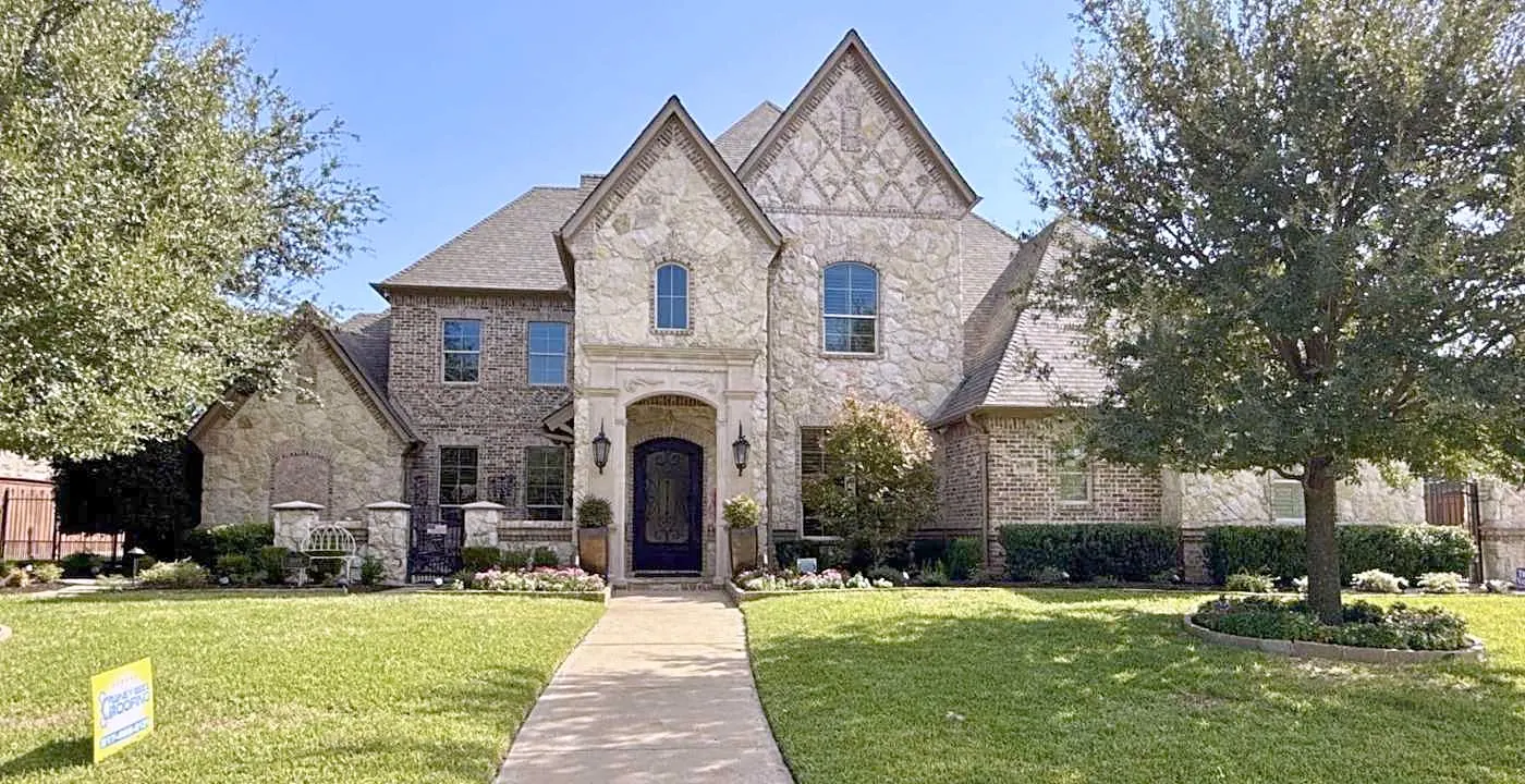 A stone and brick two-story home under a finished shingle roof, with a Honey Bees Roofing yard sign