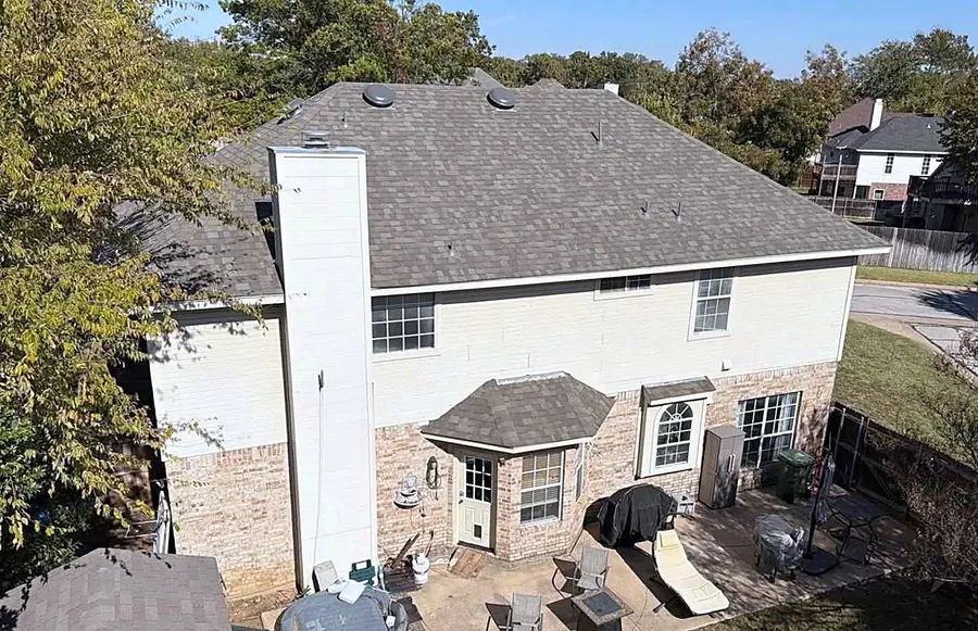A two-story home with a tall chimney under a finished shingle roof